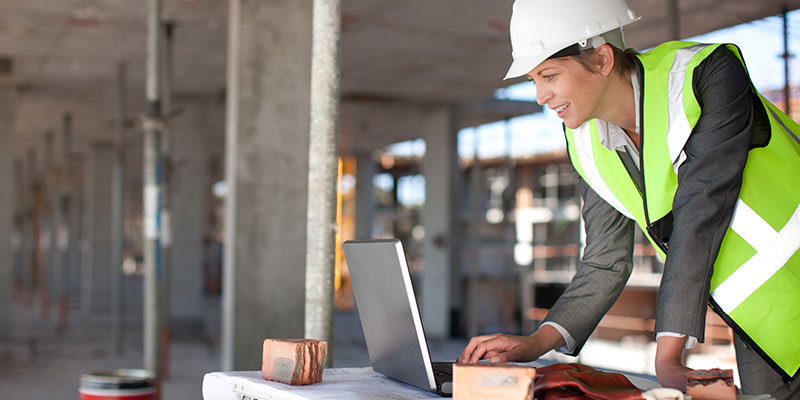 women on a construcytion site in a hard hat looking at a computer