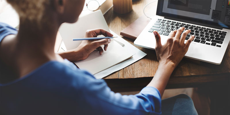 woman seated in front of laptop referring to document