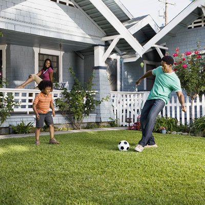 Family kicking soccer ball in yard in front of house