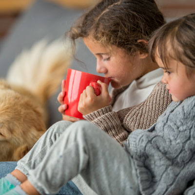 kids sitting on couch drinking cocoa with dog next to them
